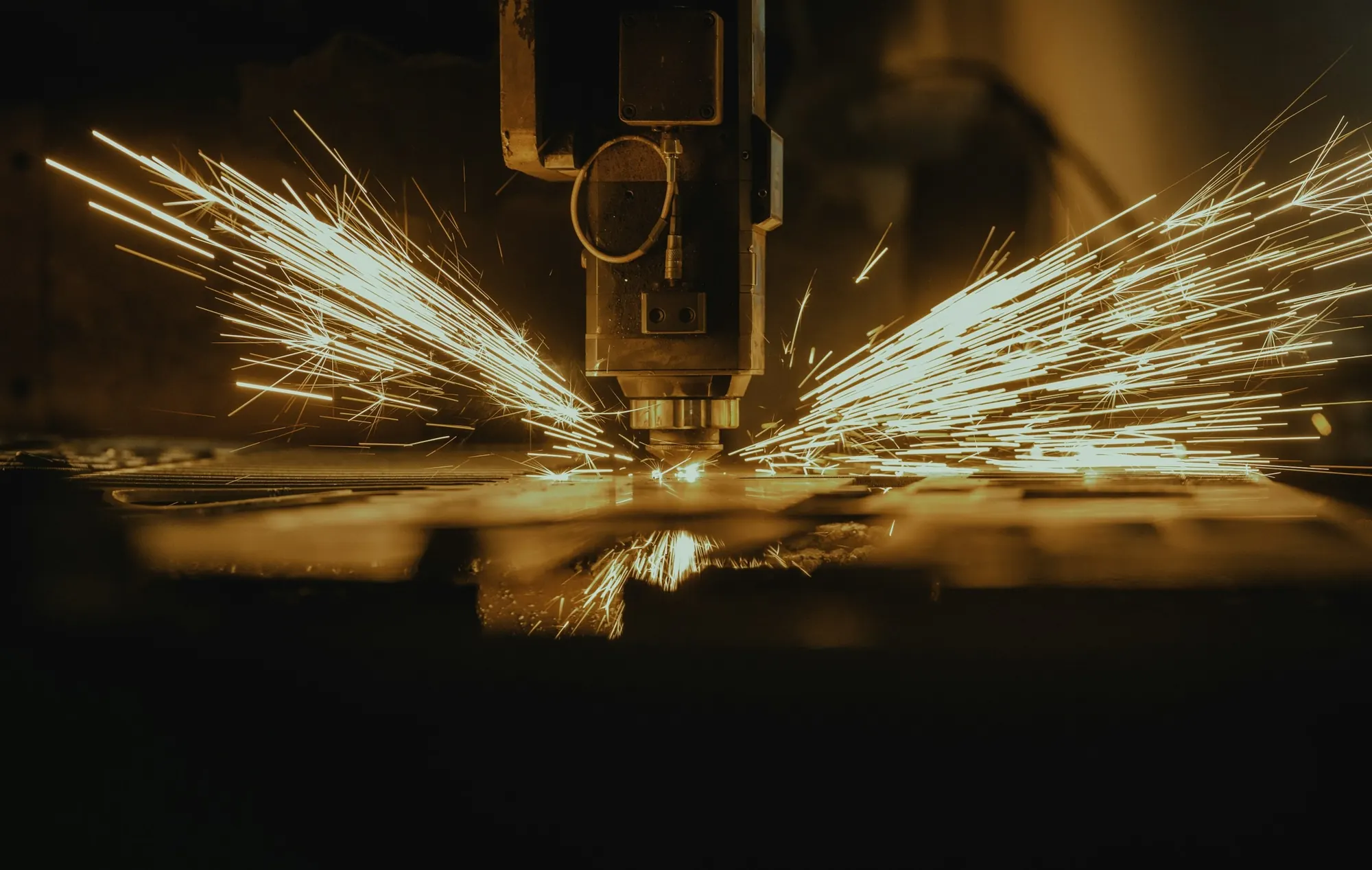 Laser cutting head throwing sparks across a metal sheet