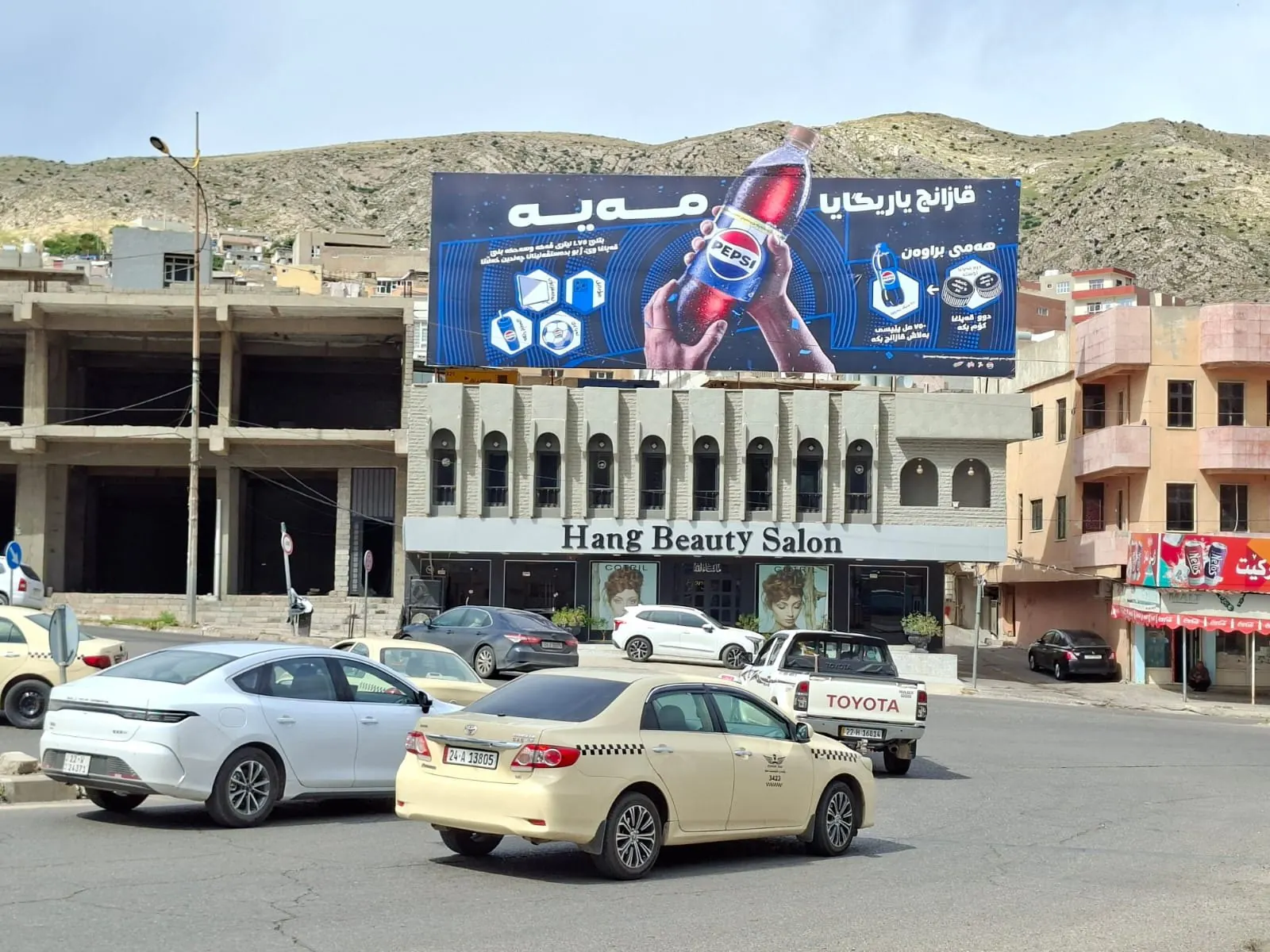 Pepsi campaign on a rooftop billboard in Duhok with mountains behind